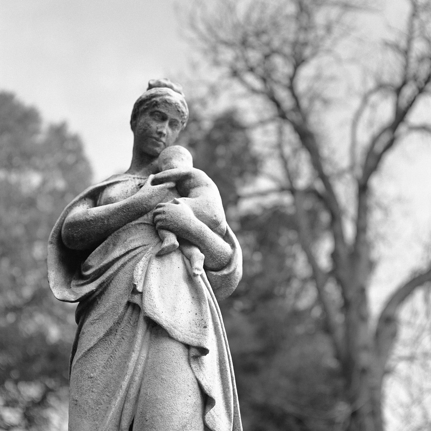 B&W image of a standing stone statuary holding a baby.