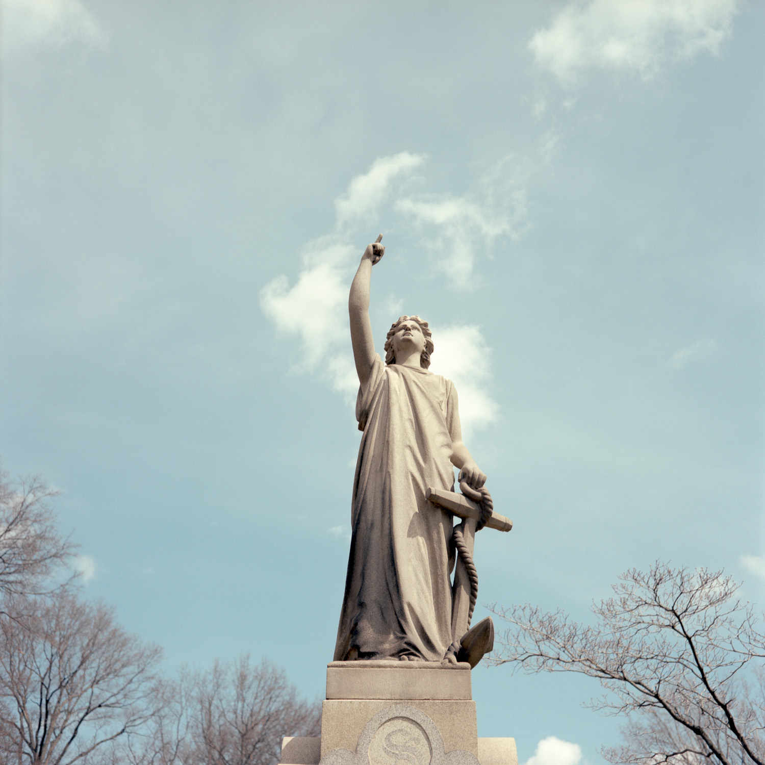 Color image of a standing stone statuary pointing up with one hand and holding an anchor with the other.