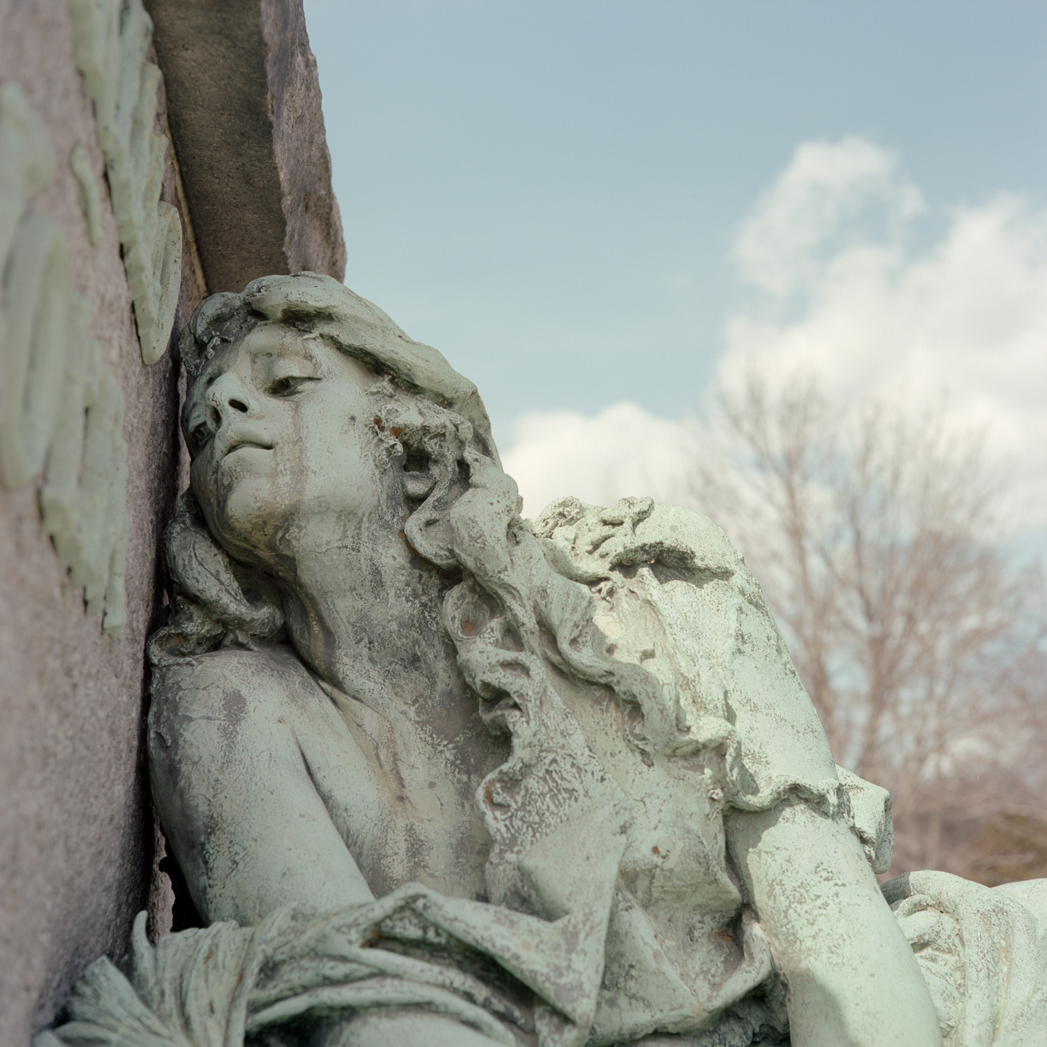 Color image of a patina bronze statuary leaning against a tombstone.