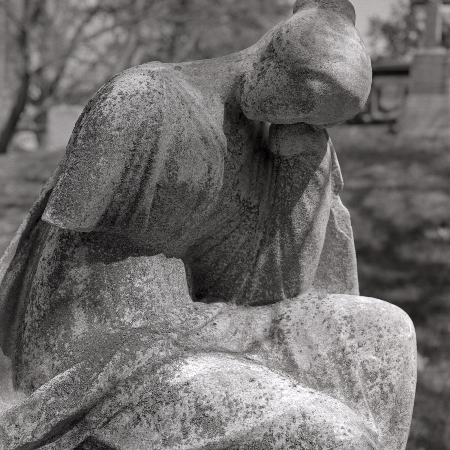 B&W image of a heavily-eroded seated stone statuary with her head resting on one of her hands.