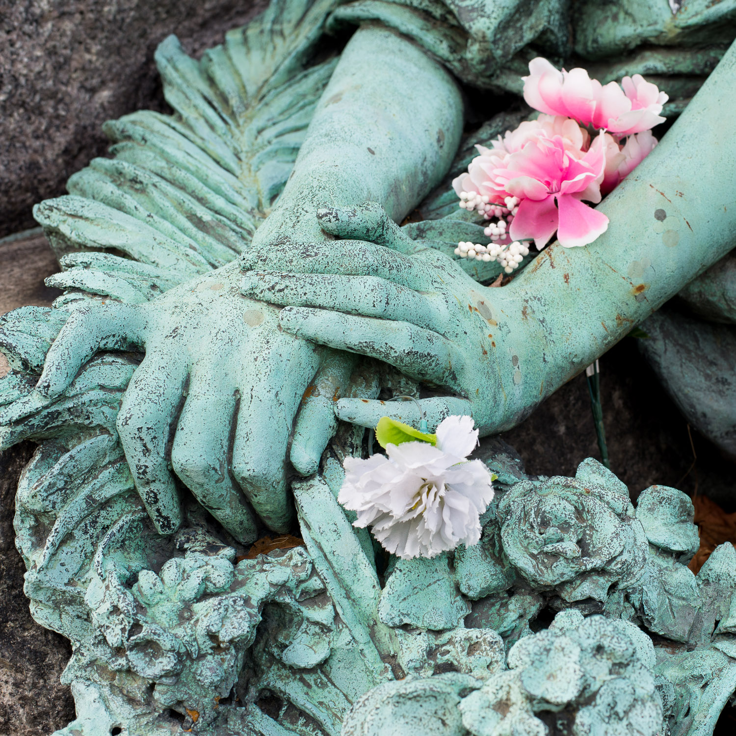 Color image of weathered bronze patina statuary hands holding real flowers.