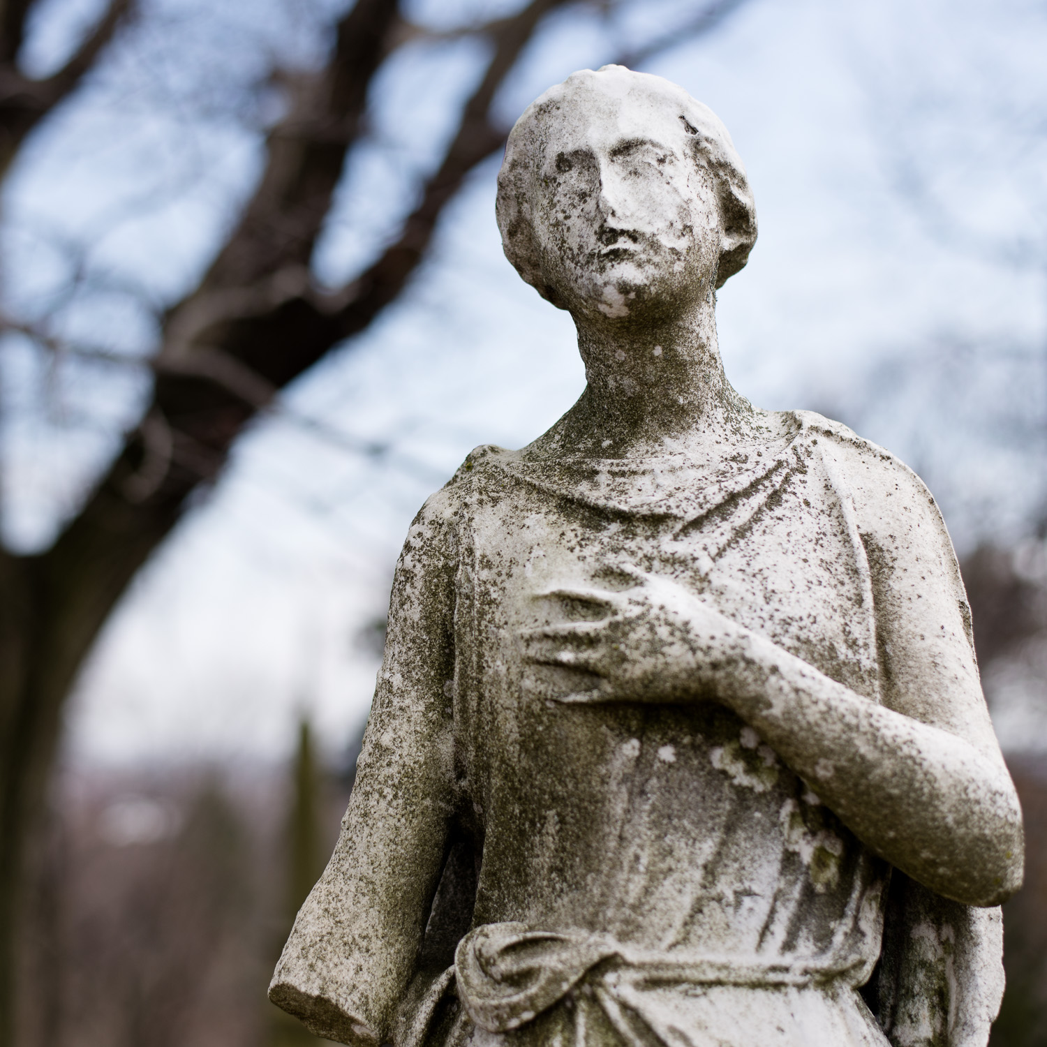 Color image of a close-up of a heavily-eroded white stone statuary with one hand on her chest.