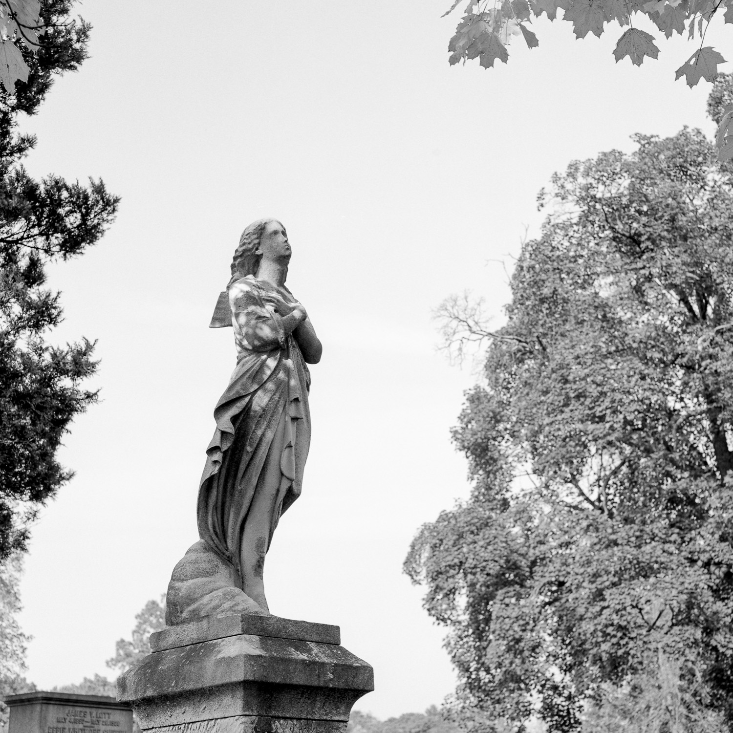 B&W image of a standing stone statuary with arms crossed on her chest.