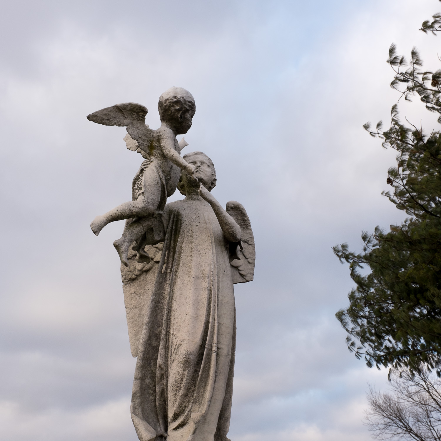 Color image of standing winged stone statuary holding a cherub over its head.