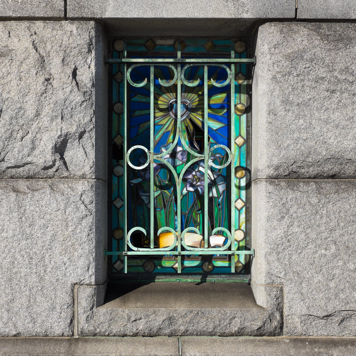 Color image of stained glass window behind green bronze bars.