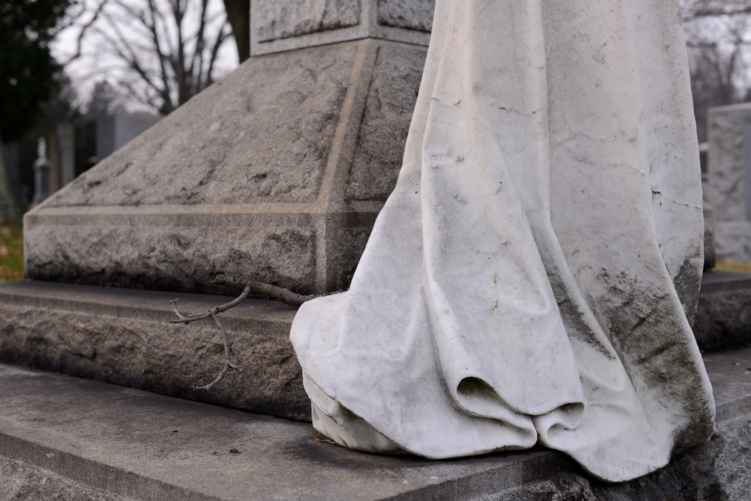 Color image of a close up of a heavily-weathered white marble skirt next to a granite tombstone.