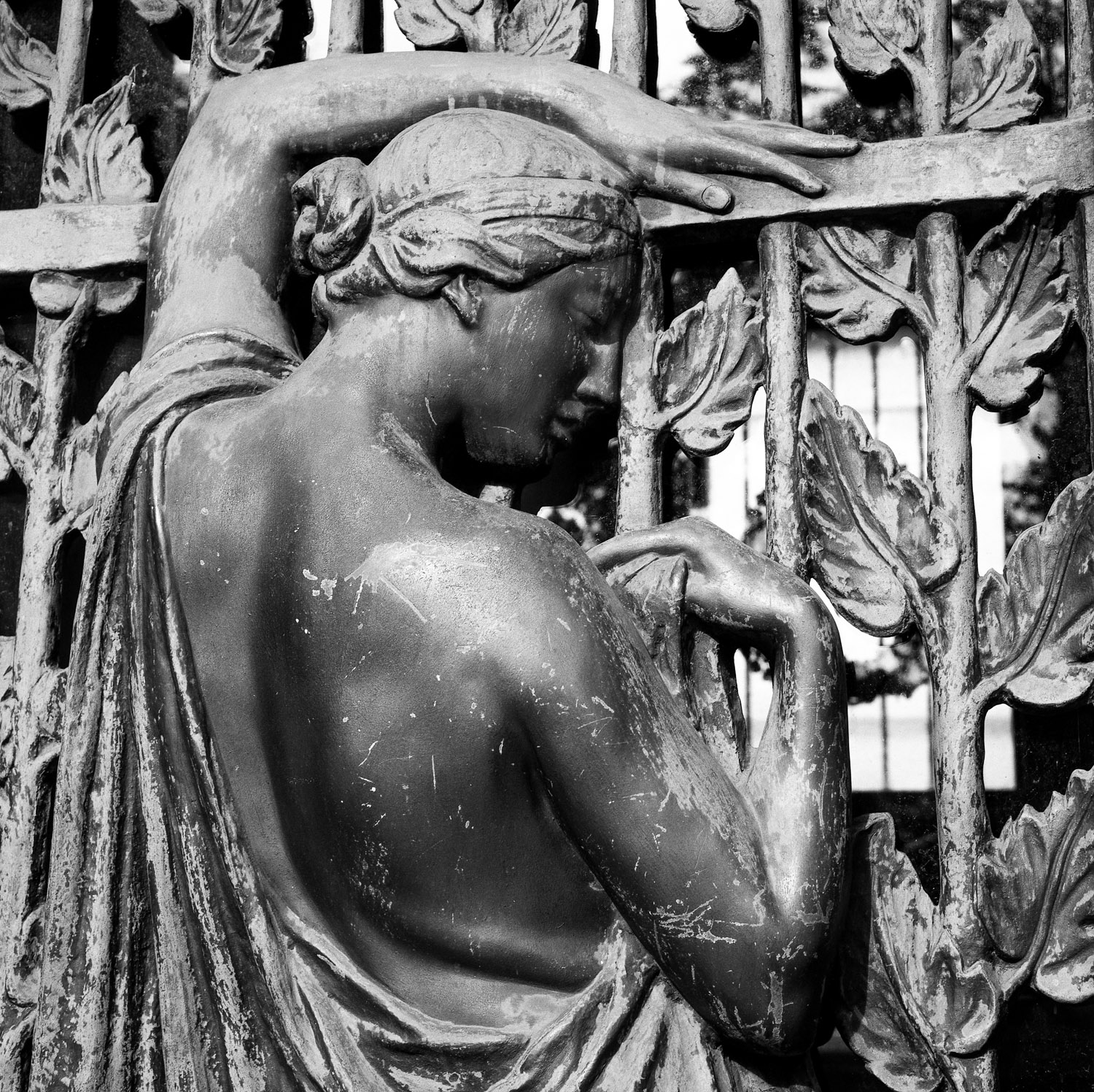 B&W image of a weathered bronze statuary with bronze leaf gate.