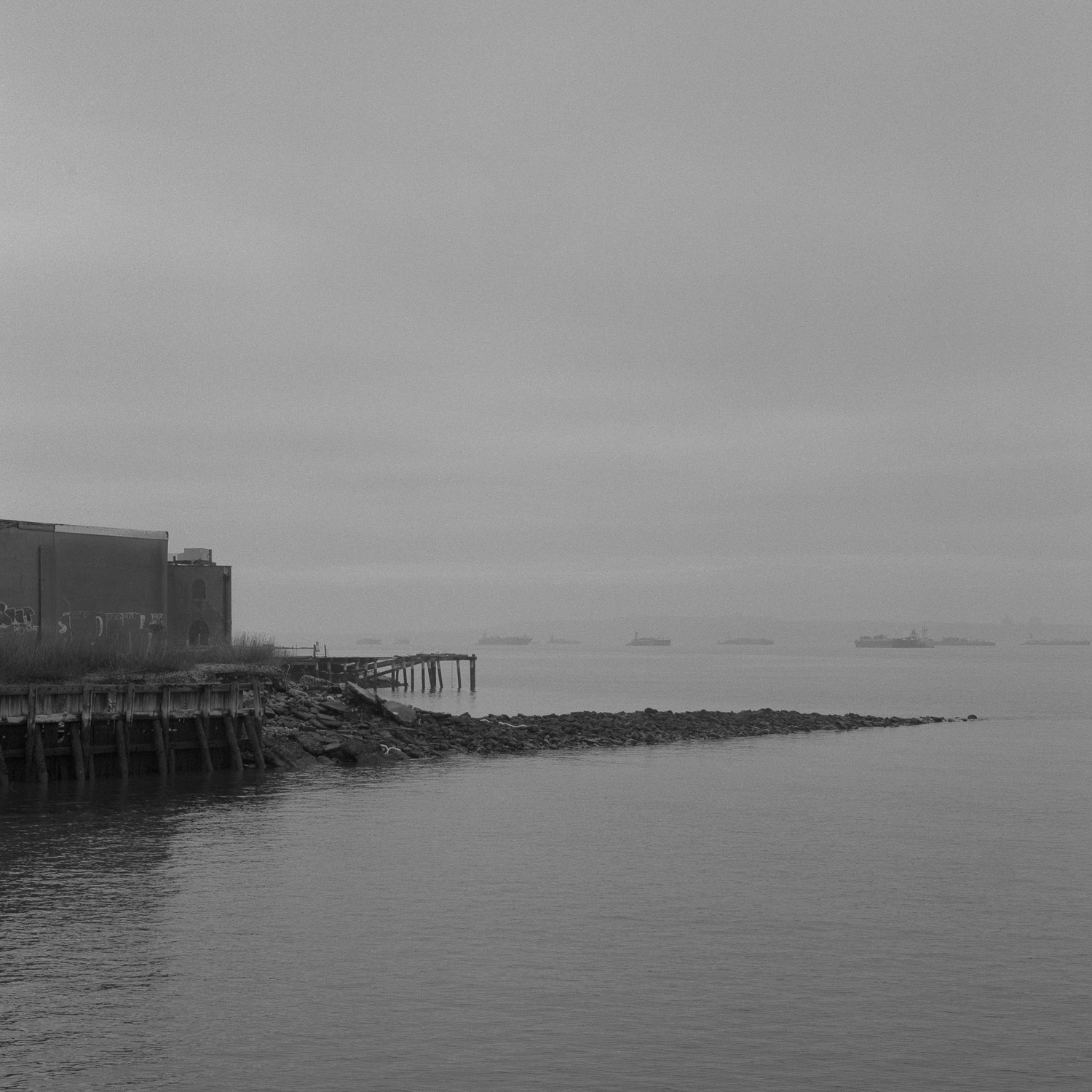 B&W image of pier in the mist with tankers in the background.