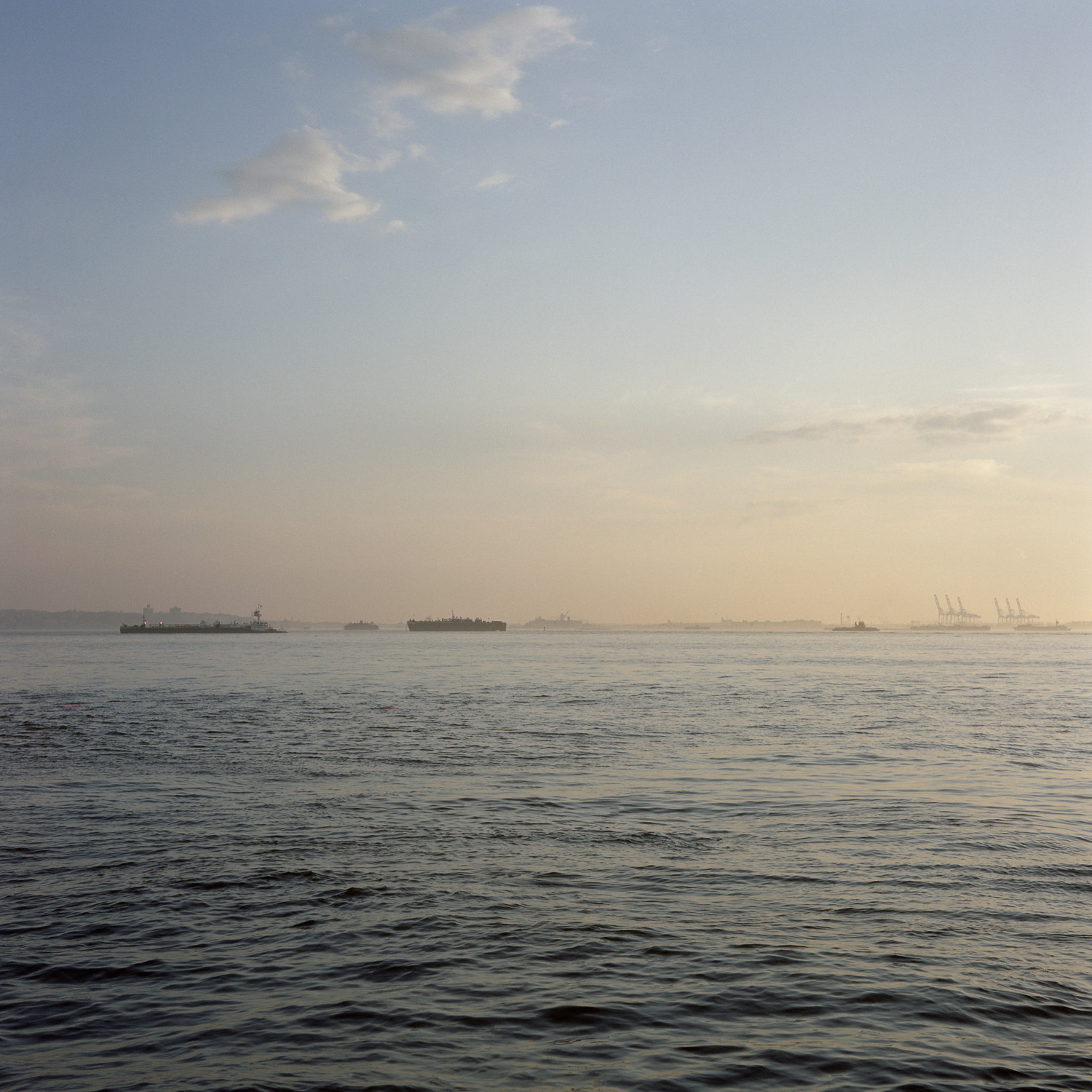 Color image of freight tankers lined up at sunset on a body of water.