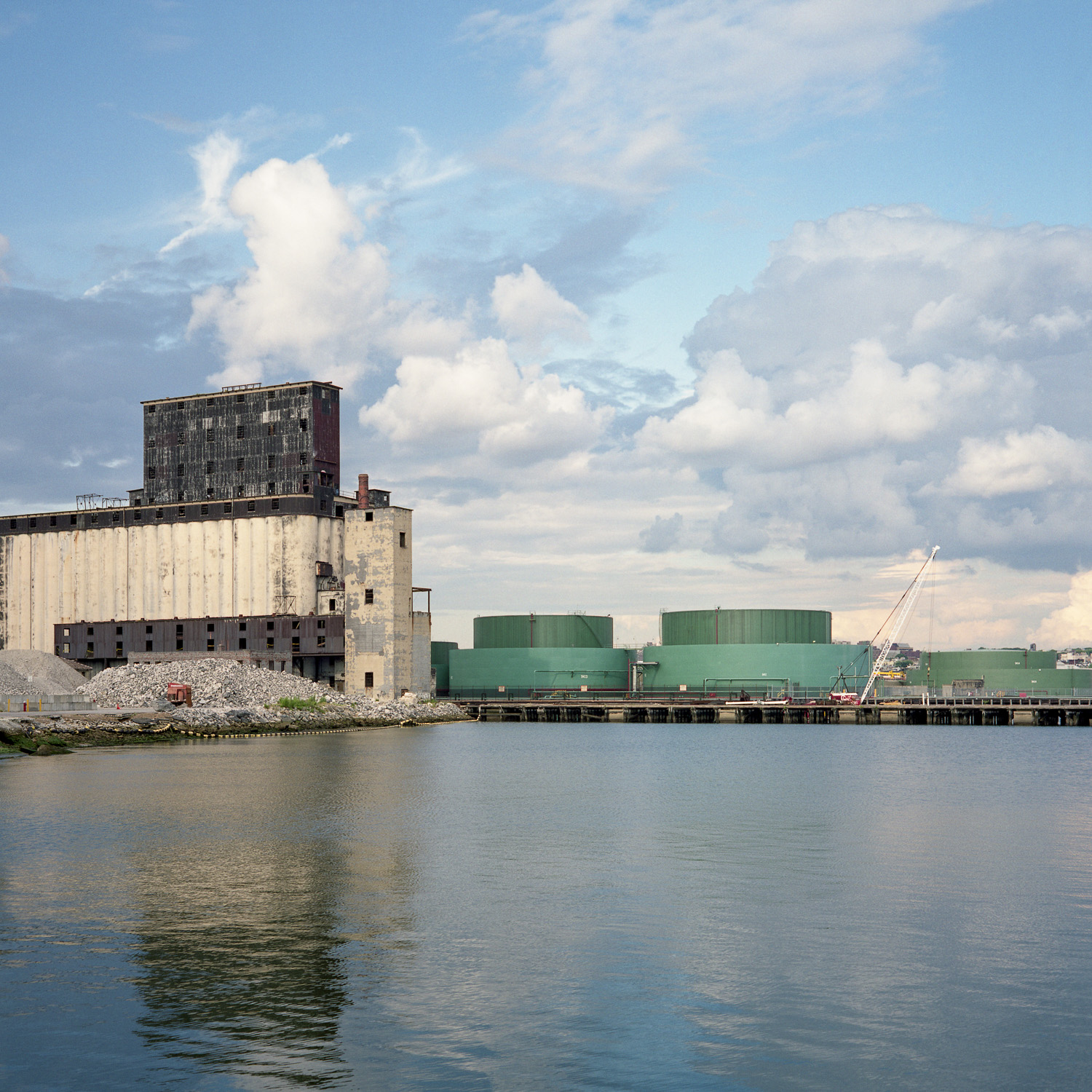 Color image of grain terminal in front of body of water under a partly cloudy blue sky.