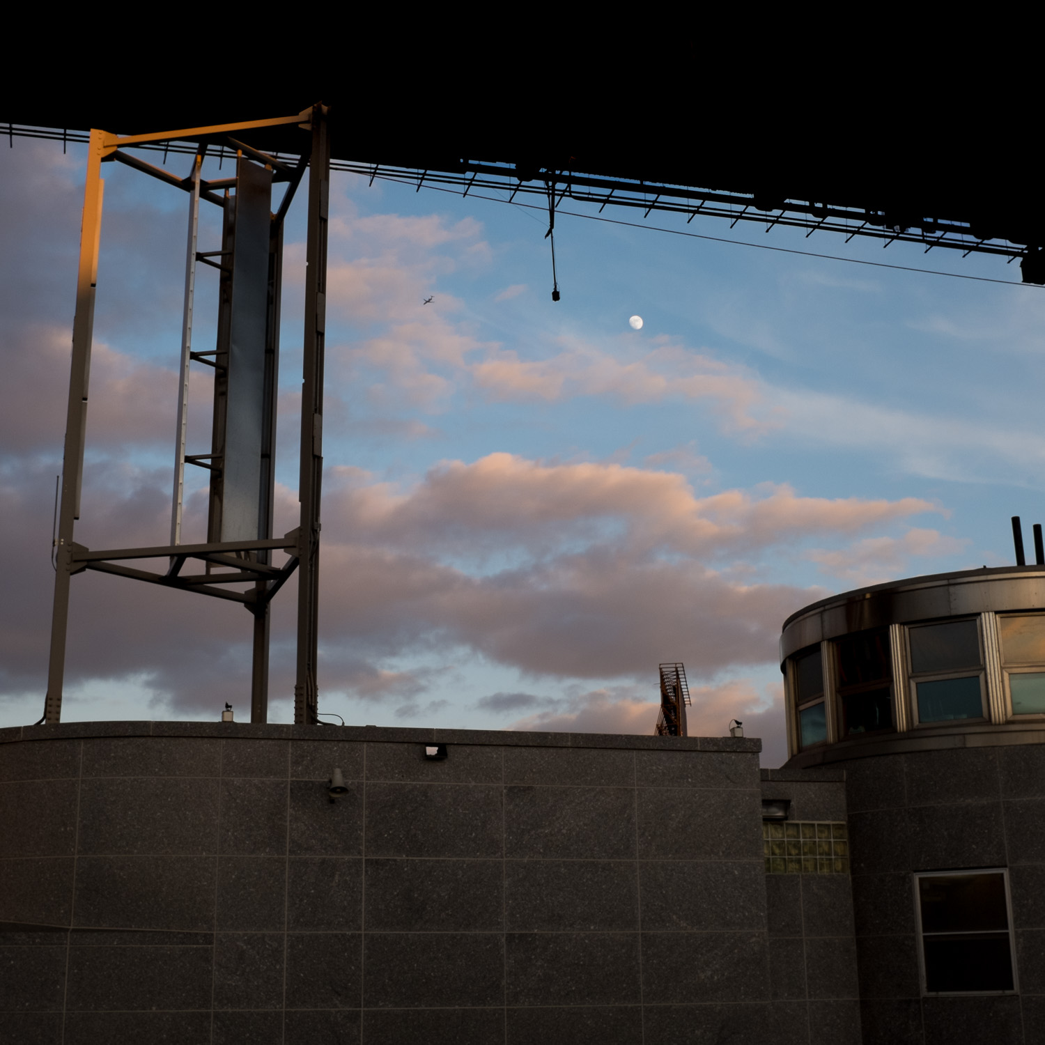 Color image of the view of a moon rising under a highway overpass at sunset.