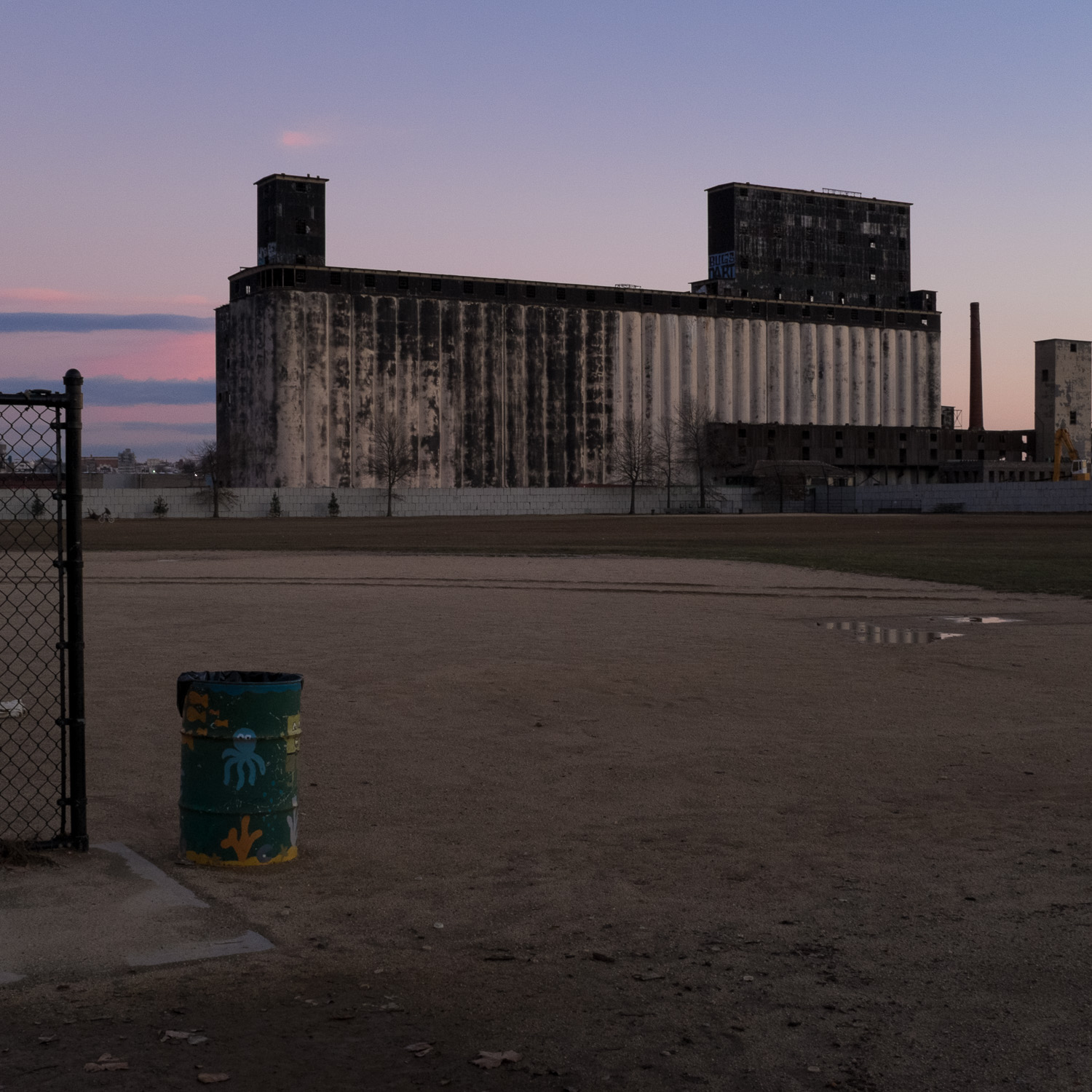 Color image of a Grain Terminal behind a baseball field right after sunset.