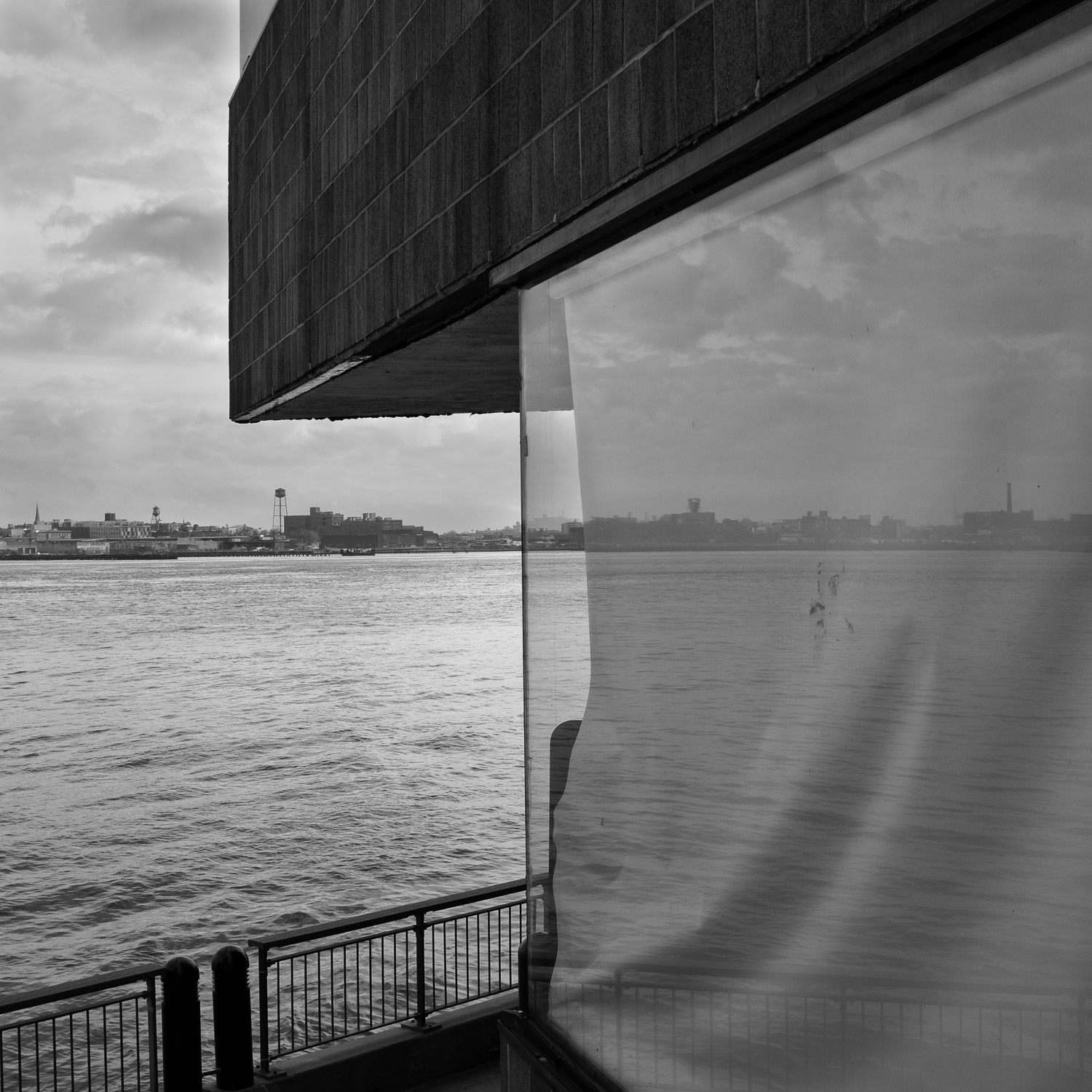 B&W image of East River bisected by its reflection in a plate glass window.