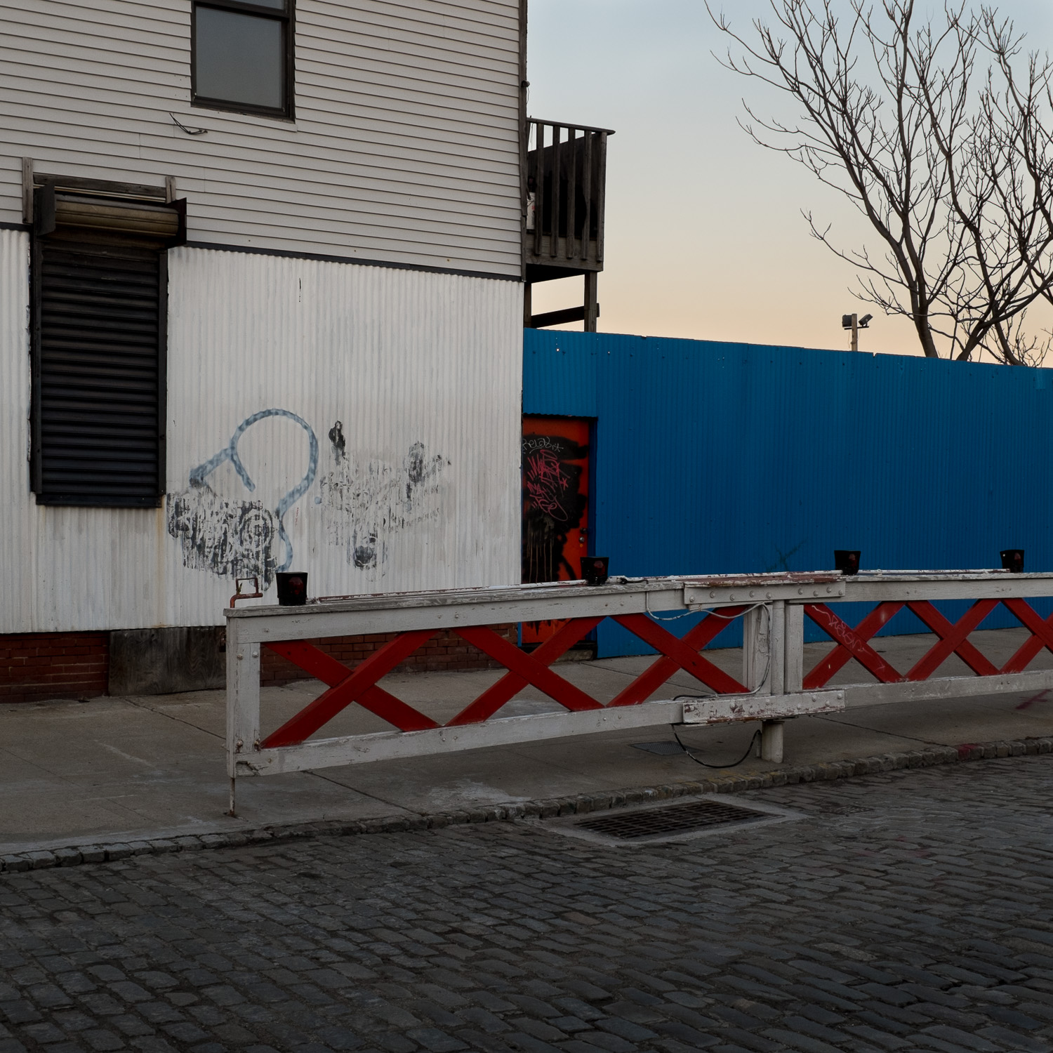 Color image of cobblestone street in front of red & white fence.