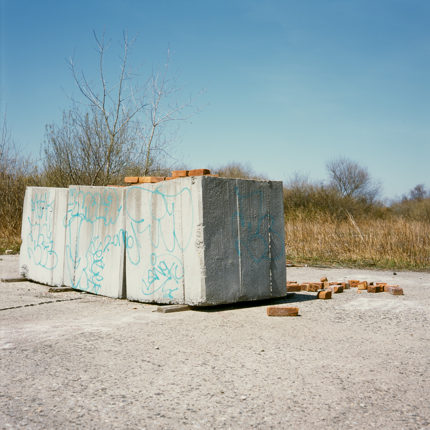 Color image of 3 large concrete blocks on a concrete foundation next to a pile of bricks.