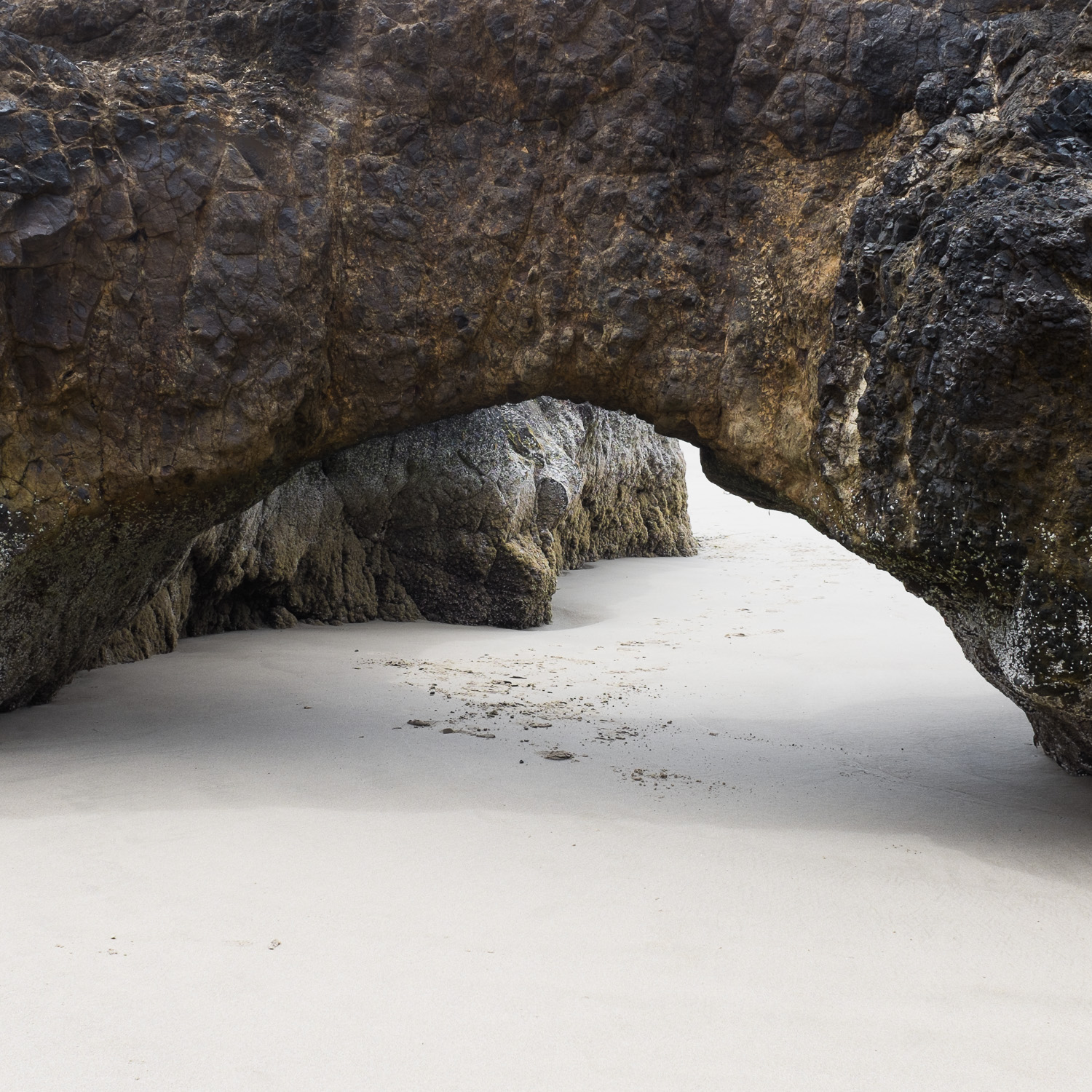 Color image of a low volcanic rock arch on a white beach