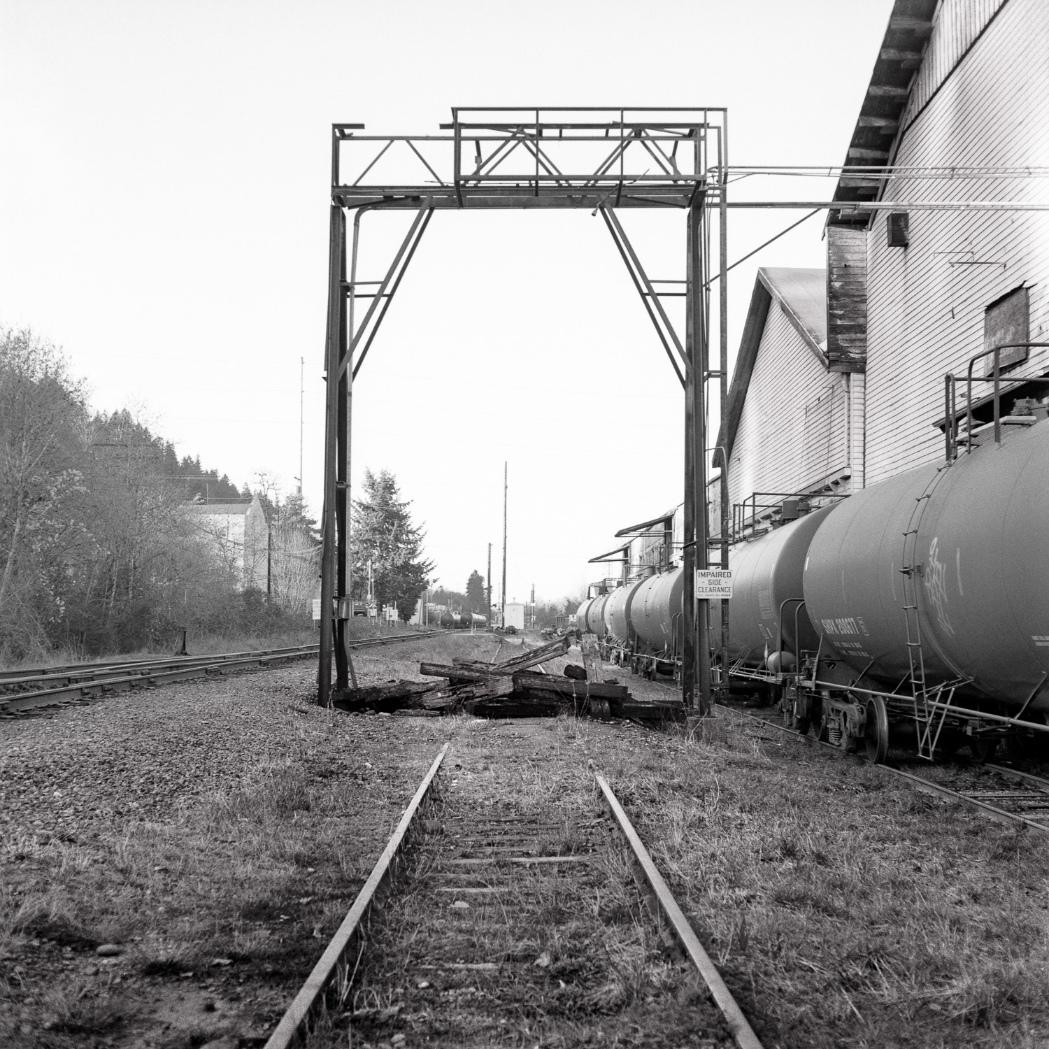 B&W image of railroad tracks leading to an old freight loader next to some oil tankers.