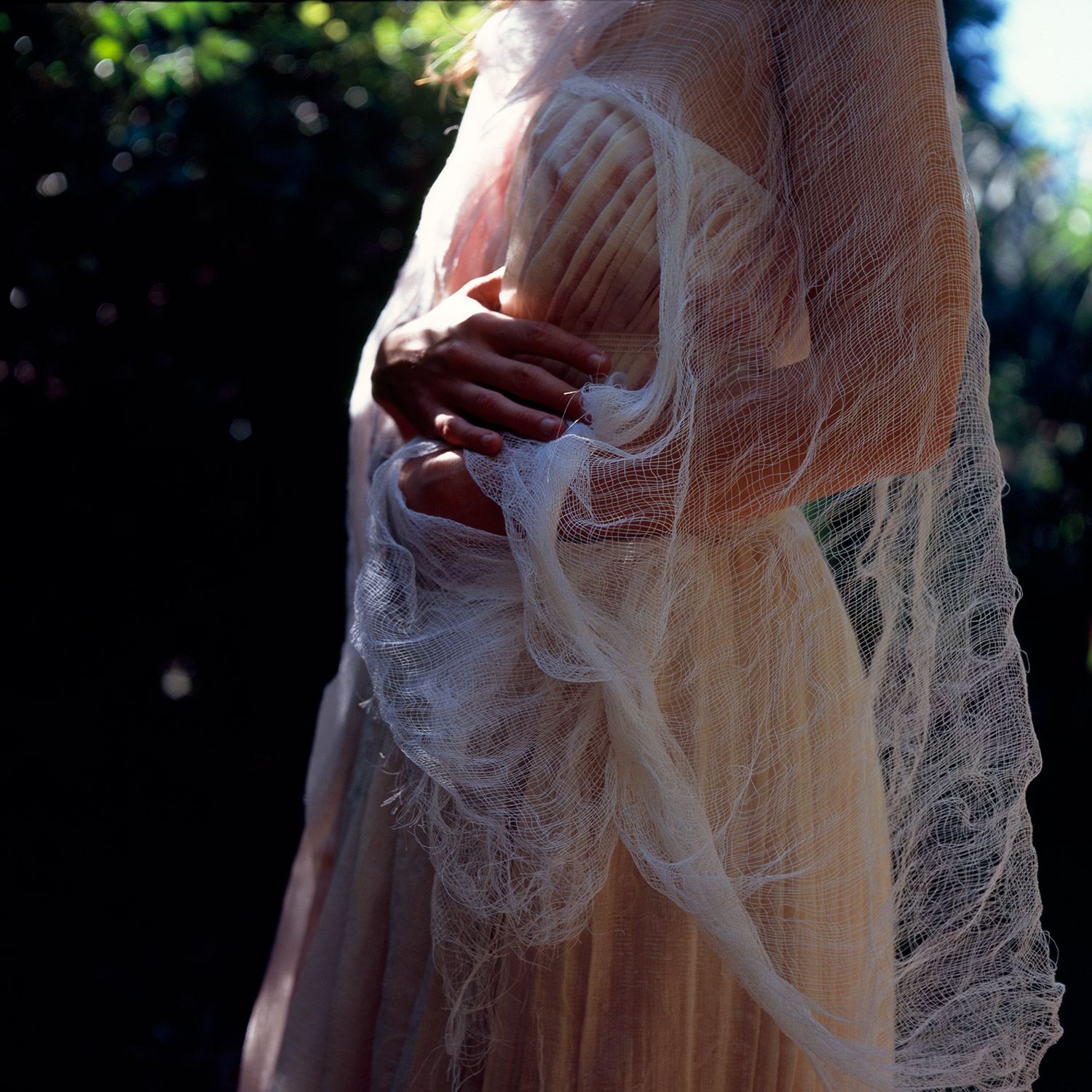 Color image of close-up of Sati avatar's hands holding her side draped with sheer netted white fabric.