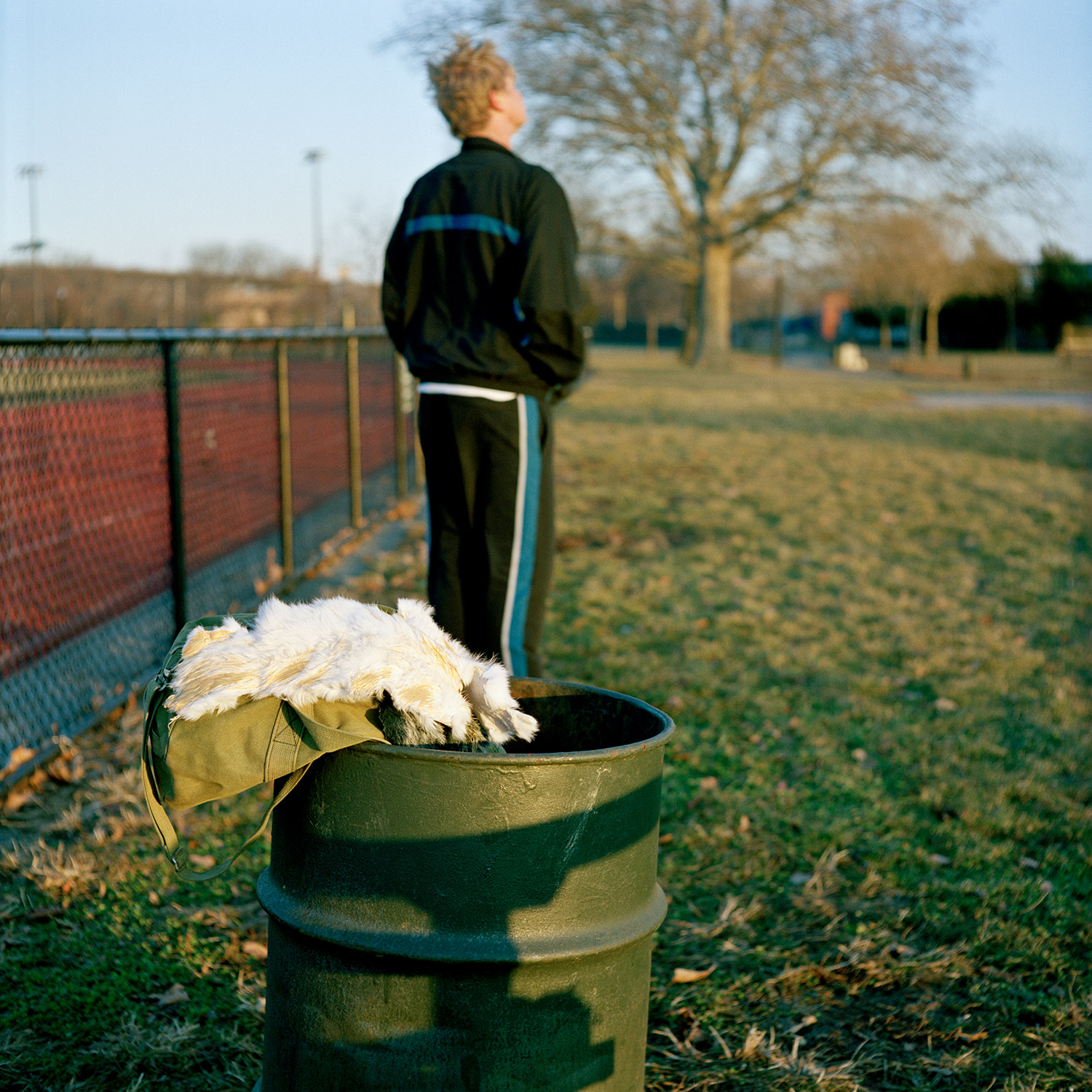 Color image of white fur pelt hanging out of a green oil drum trash can as Siva avatar looks away in the background.