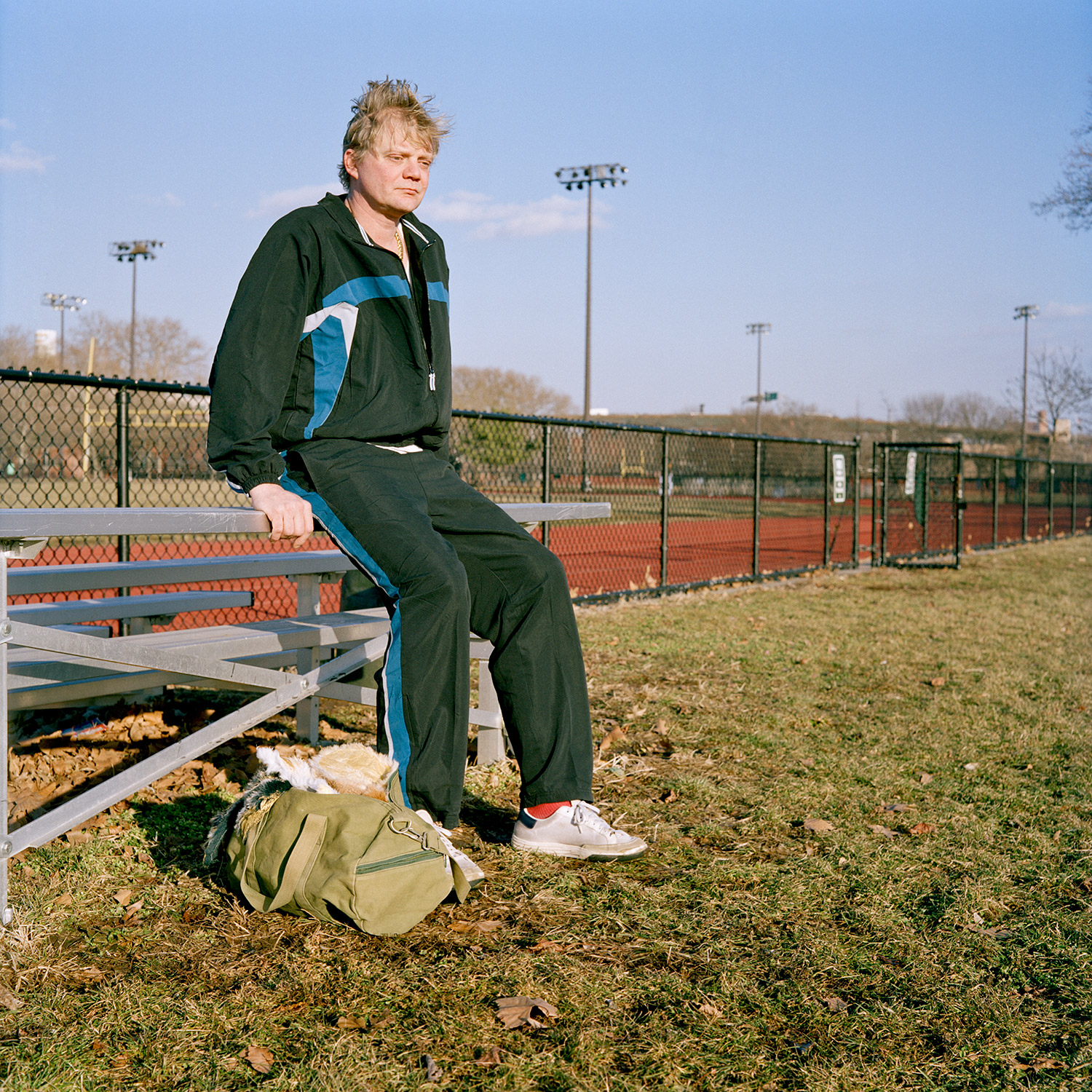 Color image of Siva avatar sitting on a bleacher, with a duffel bag holding a white fur pelt by his feet.